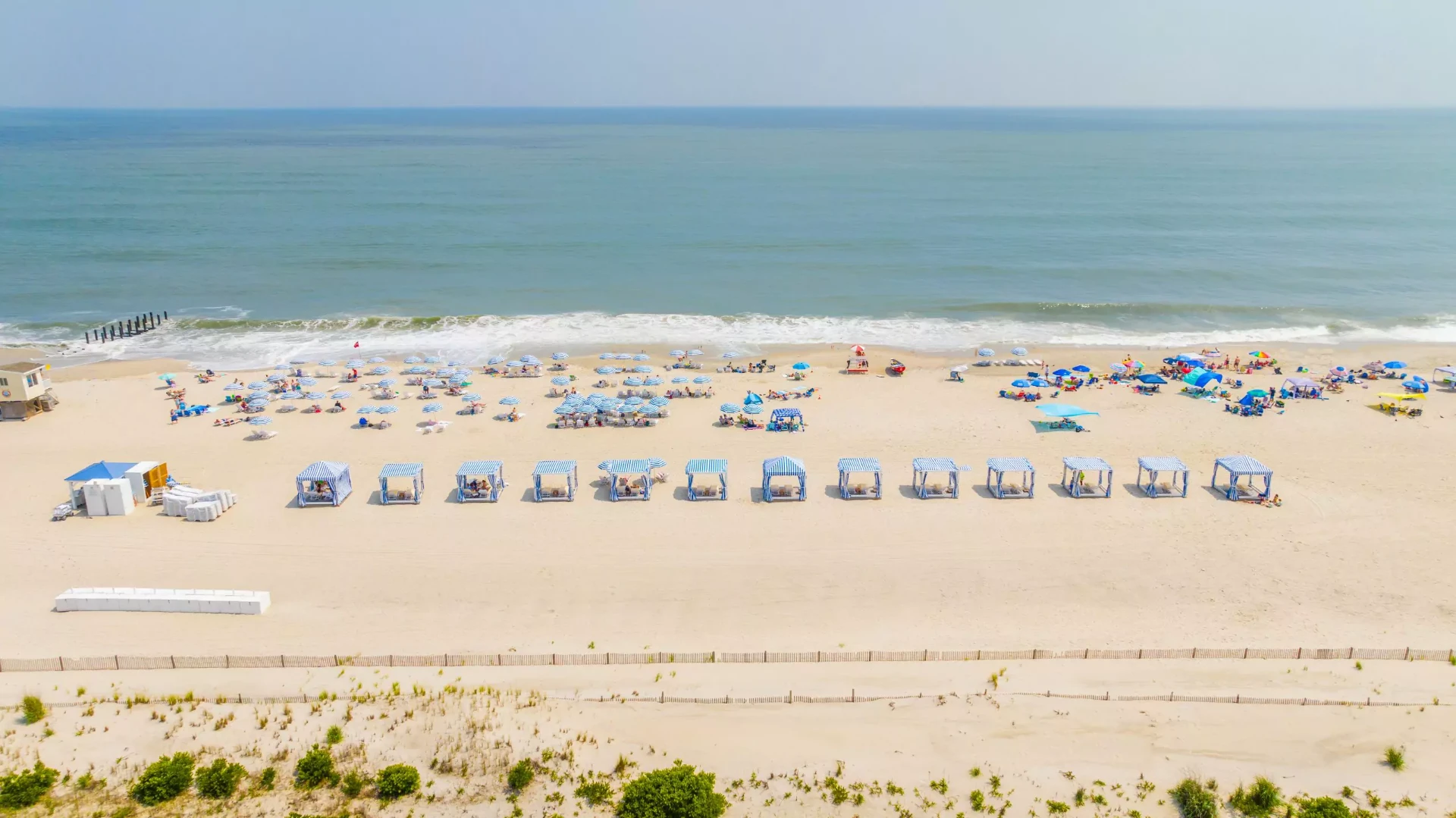 Aerial view of a busy Cape May beach with cabanas, umbrellas, and the ocean shoreline